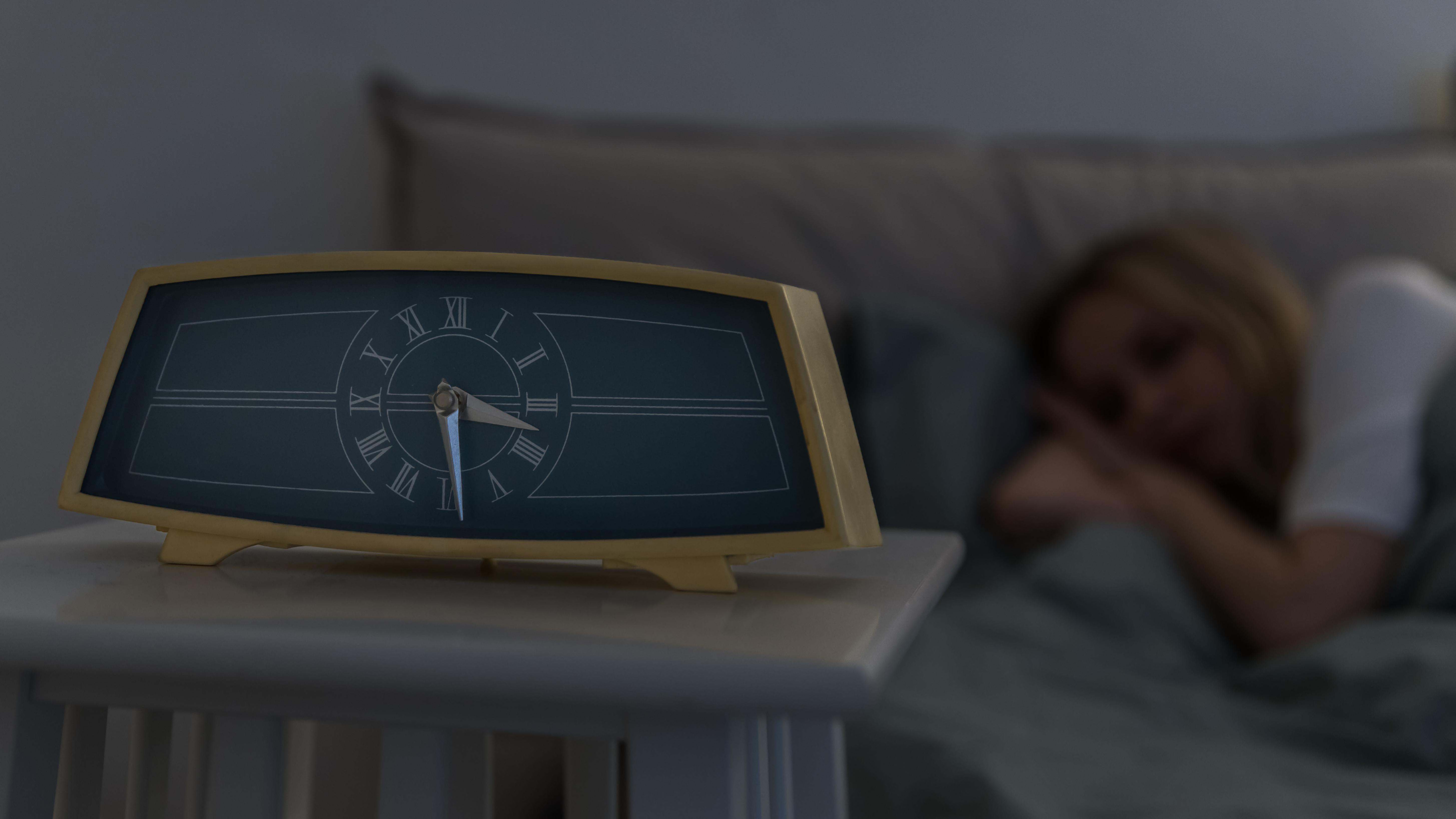 Closeup of vintage alarm clock on bedside table and calm young woman sleeping in bed