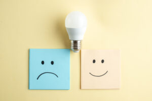 Top view of sad and smiling emoji faces on small note sheets light bulb on yellow background