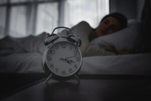 selective focus of alarm clock on bedside table near awake woman