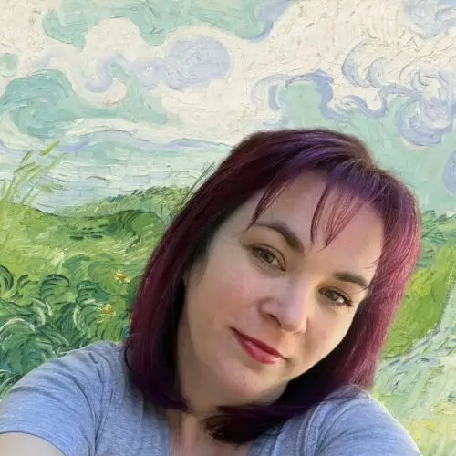 A woman with shoulder-length purple hair and a gray shirt smiles in front of a background resembling Vincent van Goghs swirling landscape painting, featuring green fields and a cloudy blue sky. STG-Health